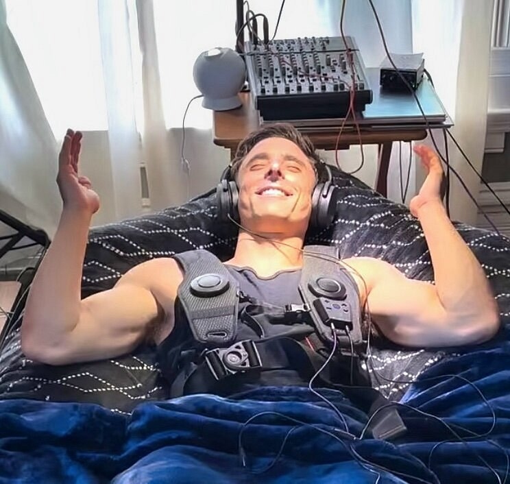 A smiling guest resting with headphones and vibroacoustic wearables